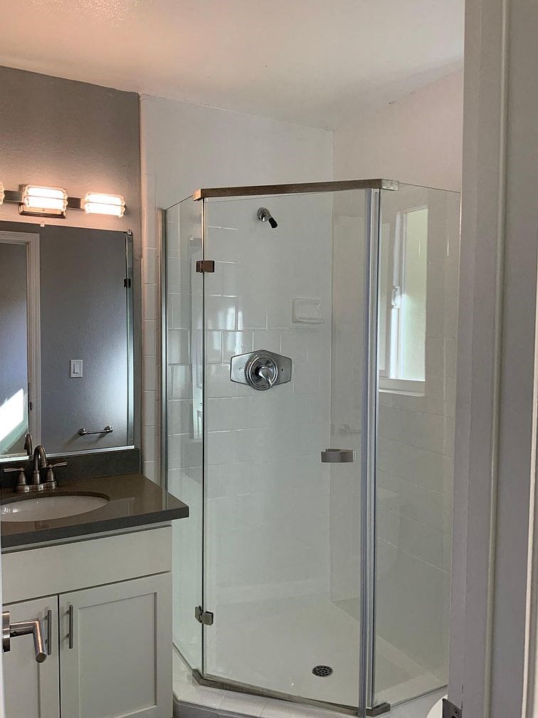 A shower with a glass door is in a bathroom with a sink and mirror.