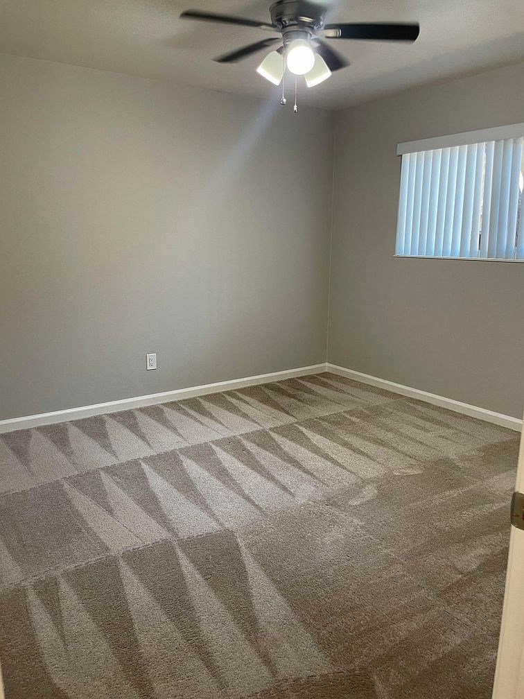 A room with a ceiling fan and carpeted floor.