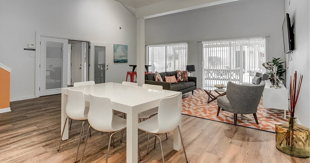 A white dining table with four chairs is in the center of a room with a wooden floor.
