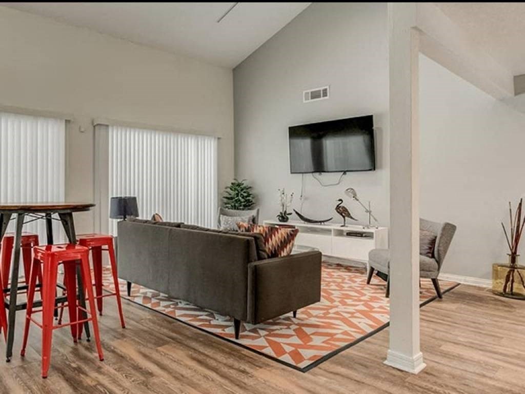 A living room with a grey couch, a television, and a wooden floor.