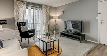 A living room with a white couch, a black chair, a glass coffee table, and a television.