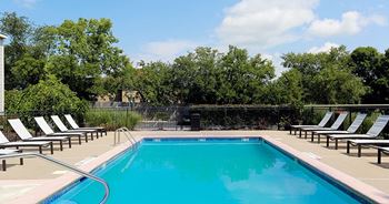 A large outdoor swimming pool surrounded by sun loungers and trees.