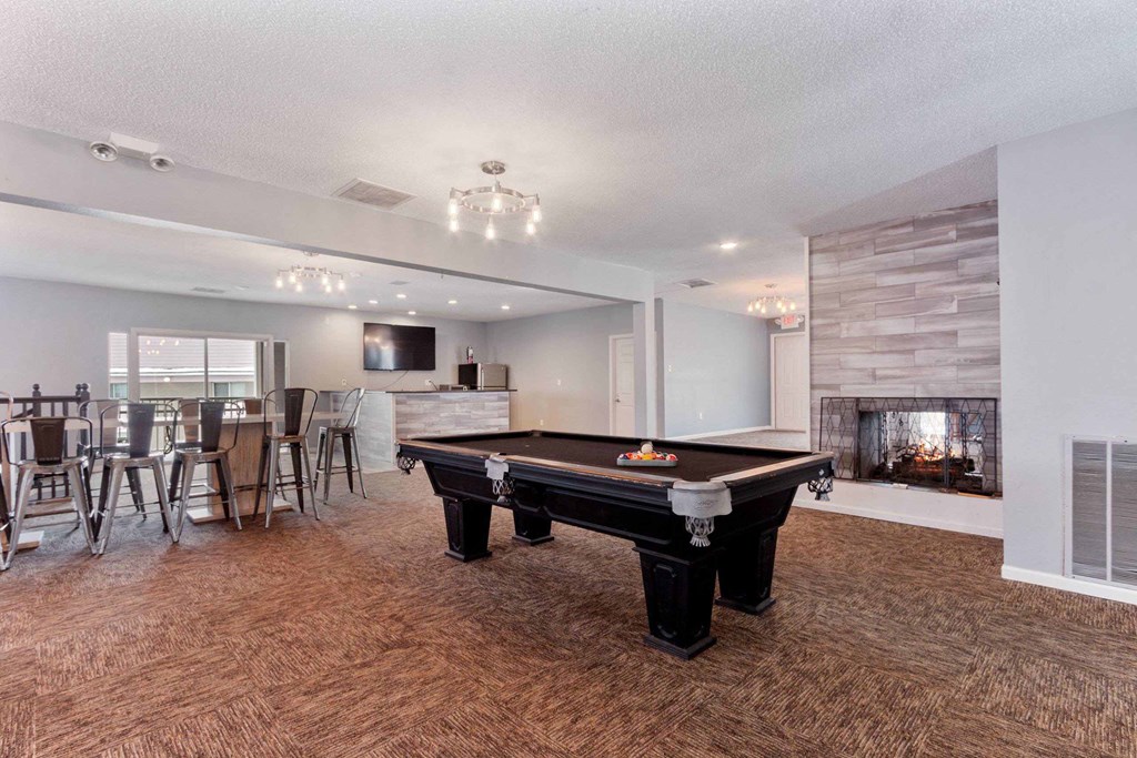 A pool table is in the middle of a room with a fireplace on the wall.