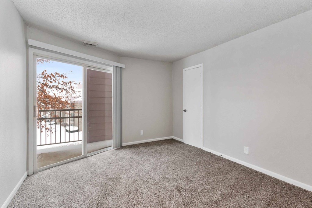 A room with a sliding glass door leading to a balcony with a railing.