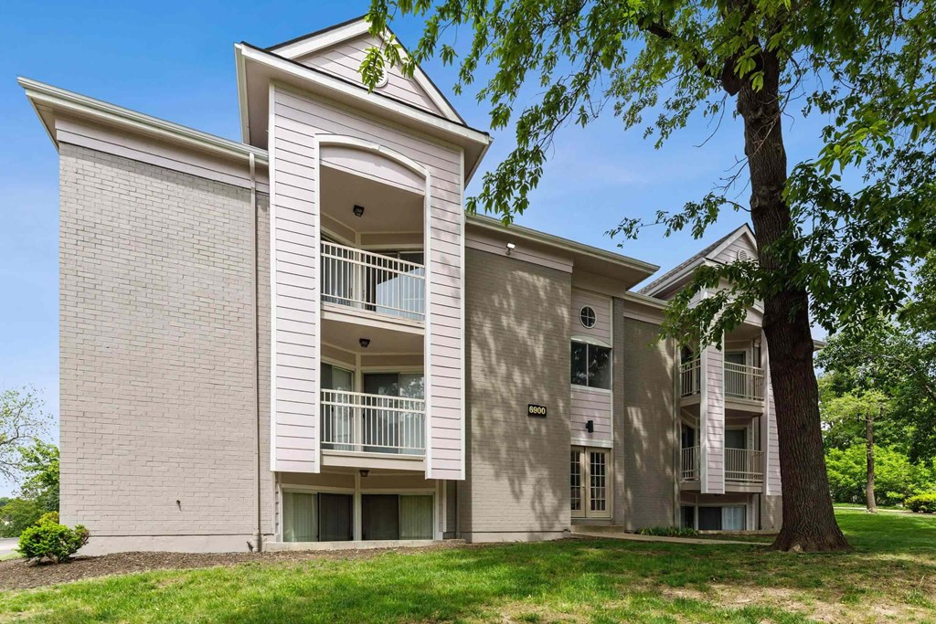 A large apartment building with a balcony and a tree in front.