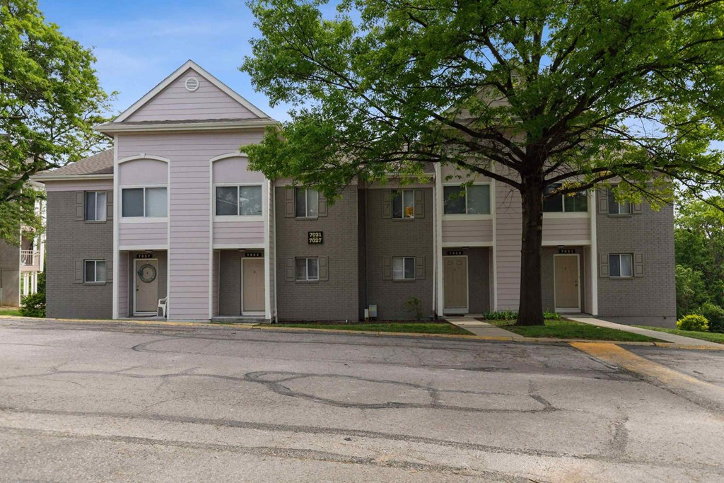 A building with grey and pink walls and a tree in front.