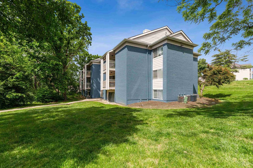 A blue building with a white roof is surrounded by green grass and trees.