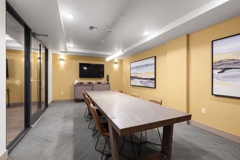 A conference room with a long table and chairs, a television, and two framed pictures on the wall.