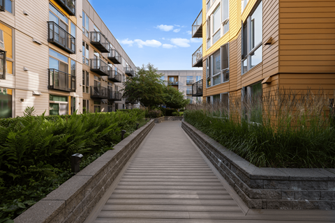 A long wooden walkway leads between two rows of modern apartment buildings.