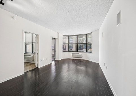 A spacious room with dark wood flooring and white walls.