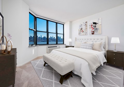 A bedroom with a large bed and a city view through the window.