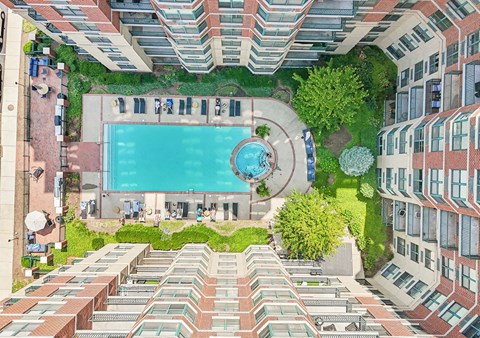 A swimming pool is surrounded by a grassy area and trees in a courtyard surrounded by buildings.