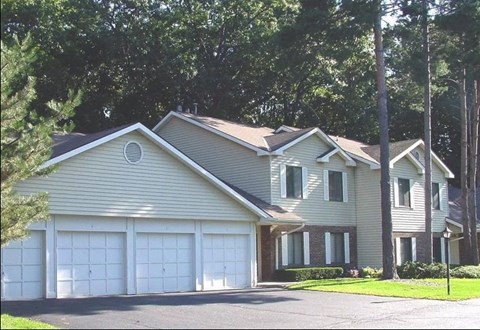 A two-story house with a garage is surrounded by trees.