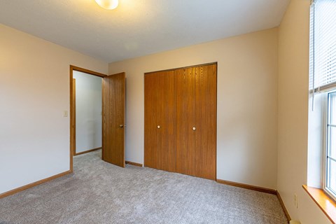 A room with a carpeted floor, two wooden doors, and a window with blinds.
