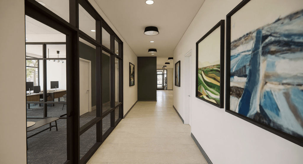 A hallway with a painting on the wall and a table with chairs on the left.