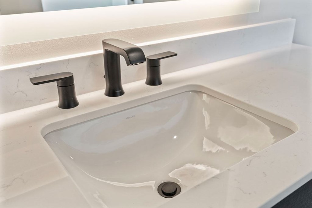 A white sink with two faucets is on a white countertop