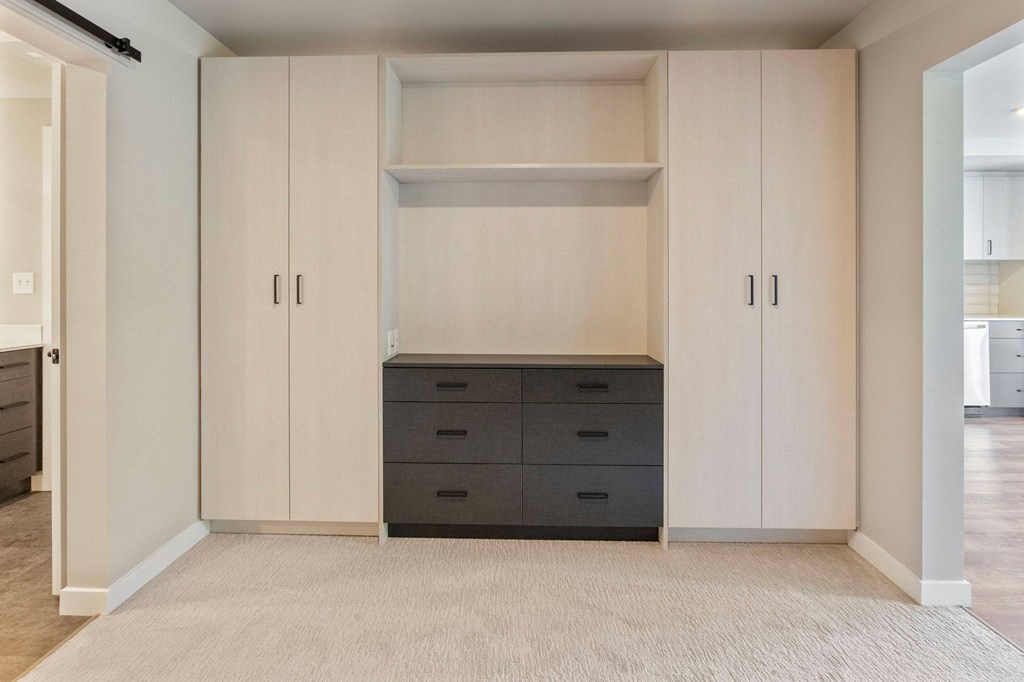 A room with a white carpet and a black dresser with a cabinet above it.