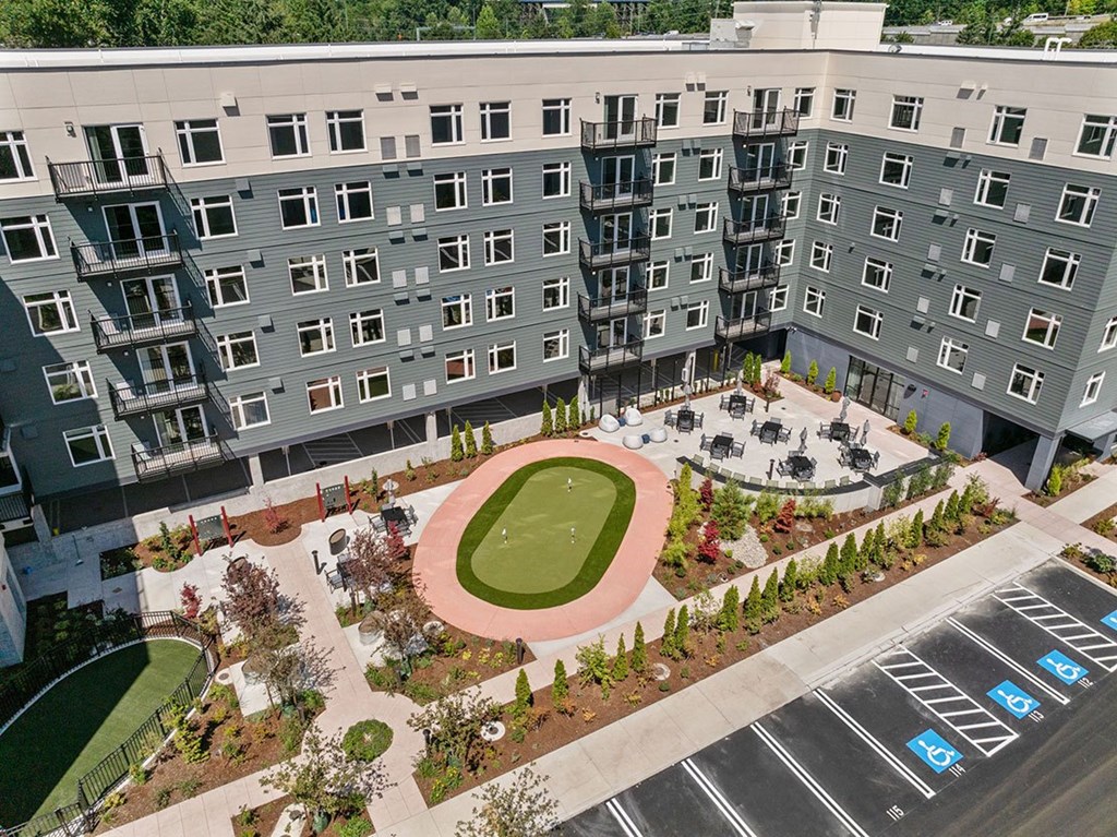 A large apartment complex with a green lawn and a fenced-in dog park