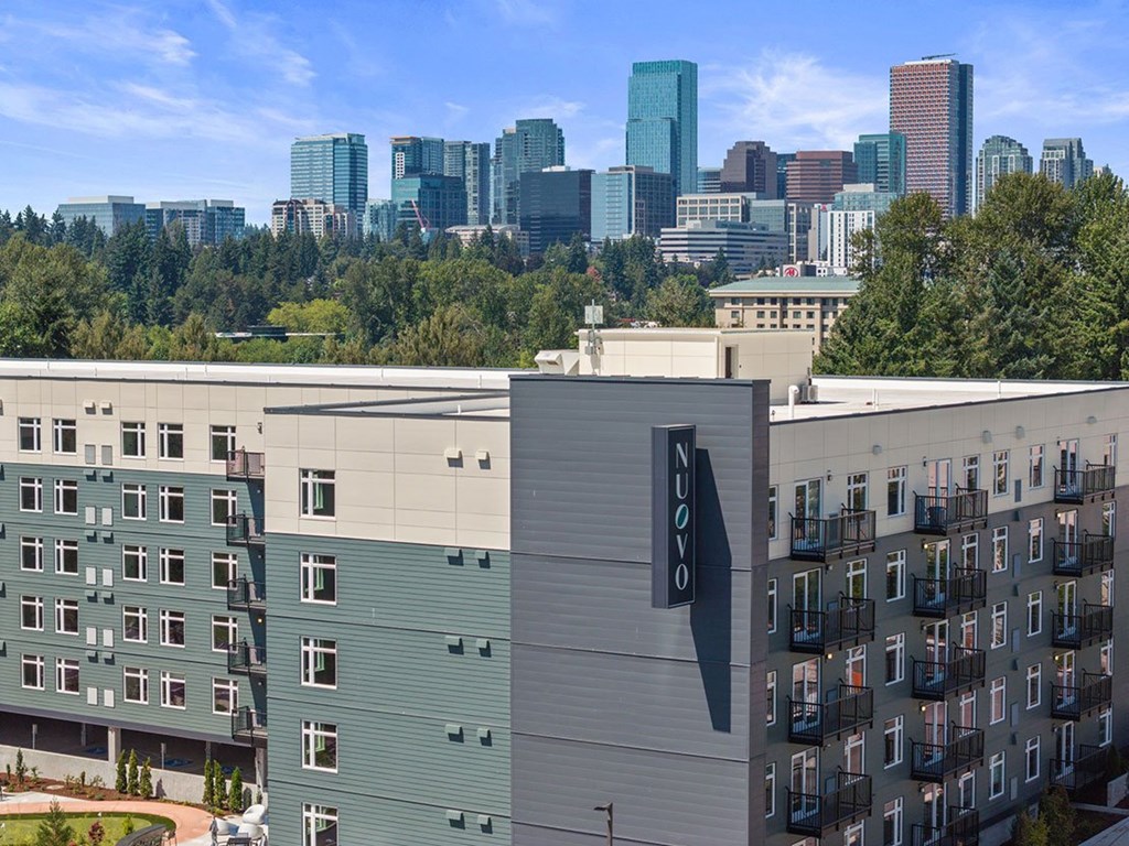 A modern building with a large sign on the sides is in the foreground with a city skyline in the background