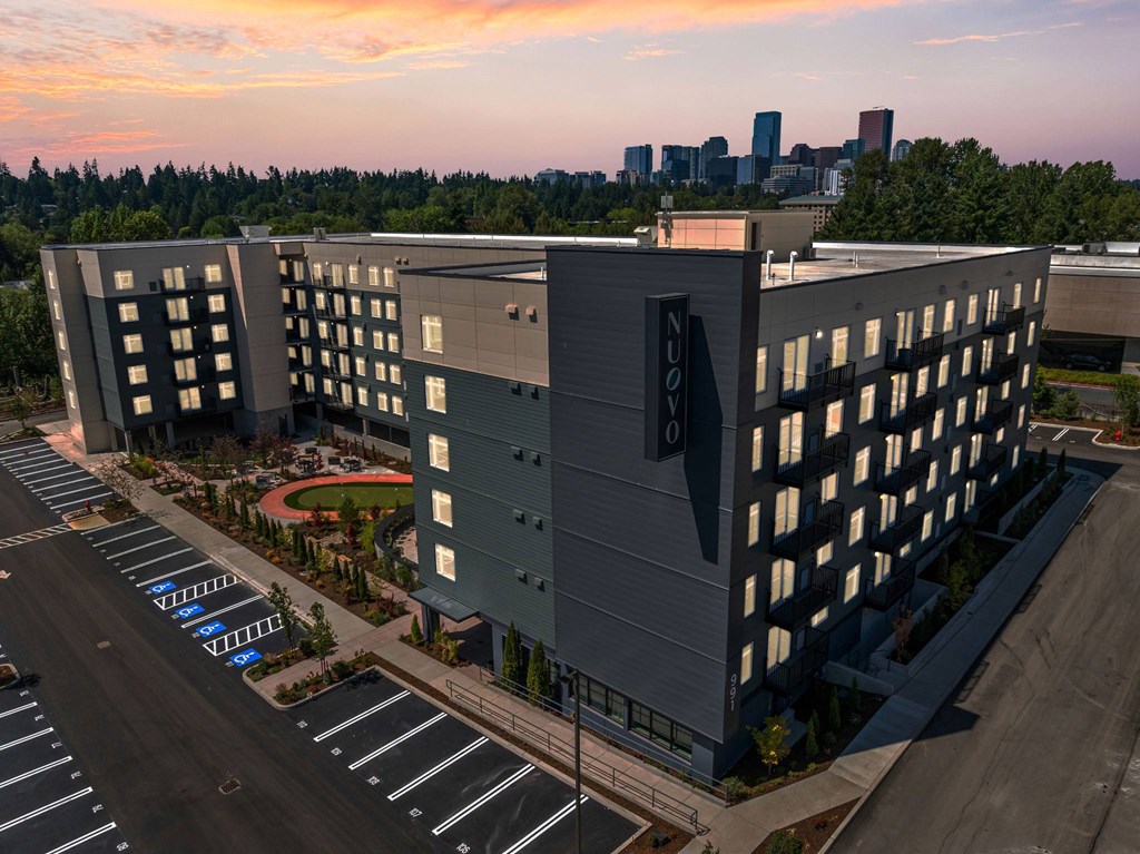 A parking lot in front of a large building with a city skyline in the background