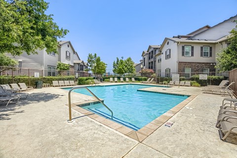 A swimming pool surrounded by lounge chairs and trees in a residential area.