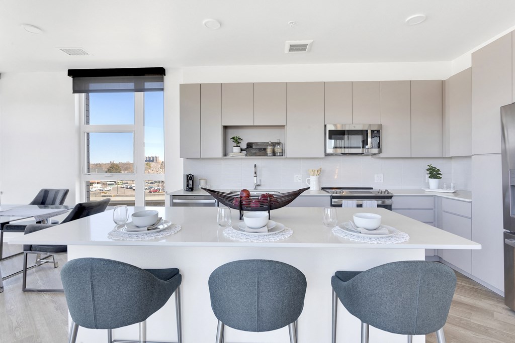 a kitchen with white cabinets and a large island with a white countertop and four blue chairs