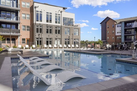 A modern pool with a unique design is surrounded by contemporary buildings.