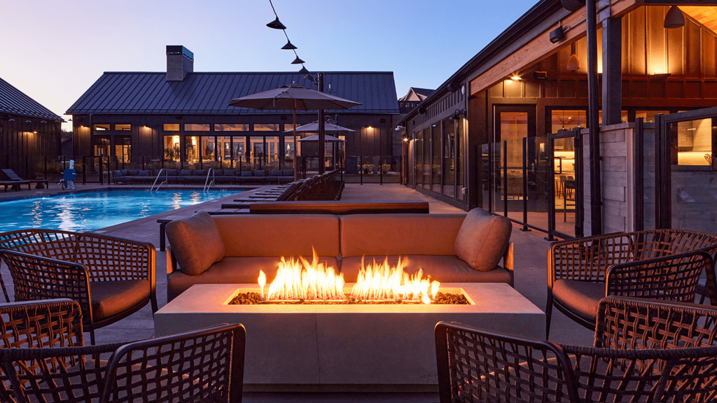 a lounge area with a fire pit and a pool at night