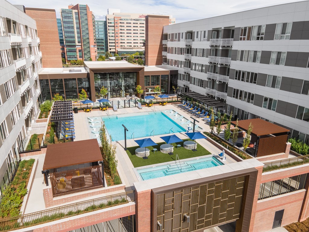 A large swimming pool surrounded by a patio area with lounge chairs and umbrellas.