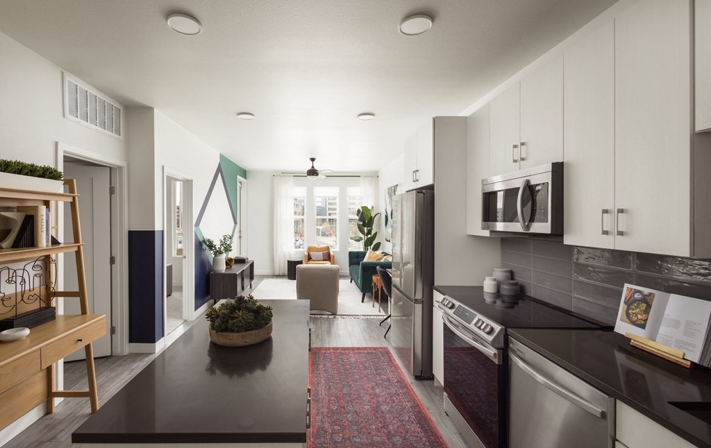 a kitchen and living room with white cabinets and a black counter top