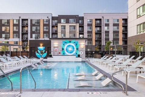 A large pool surrounded by lounge chairs in front of a building.