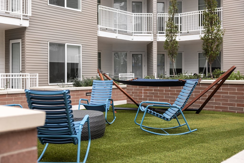 Three blue chairs are placed on a lawn in front of a building.