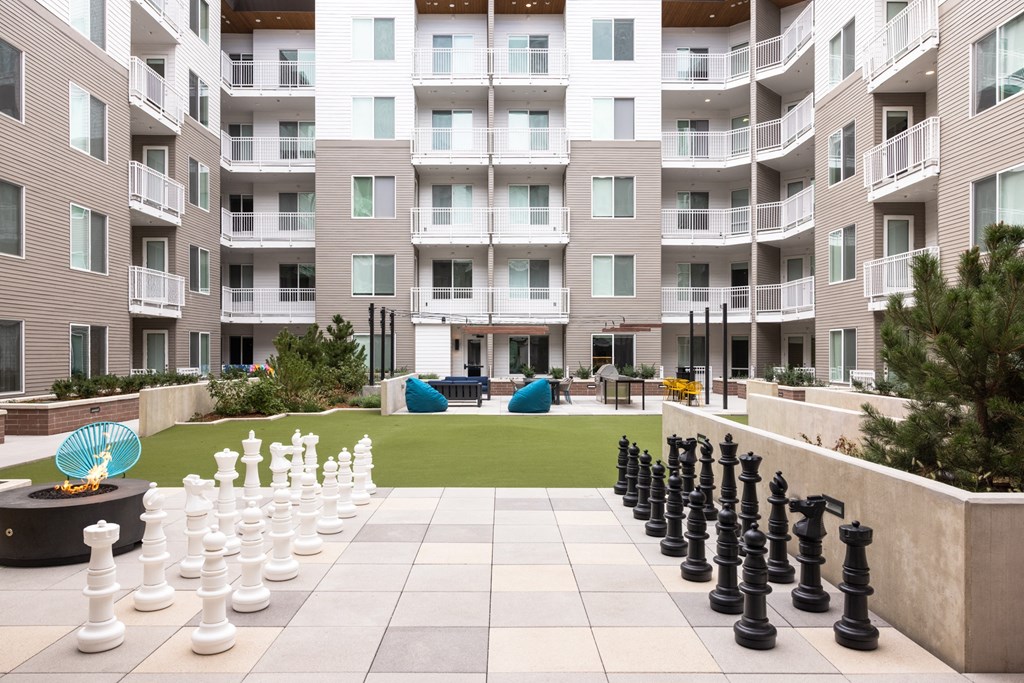 A giant chess set is set up on a patio in front of apartment buildings.