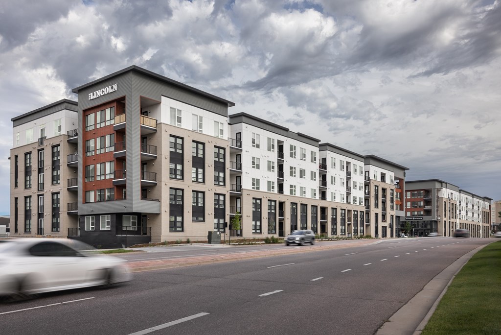 A white car is driving down a street past a building with a sign that says Lincoln.