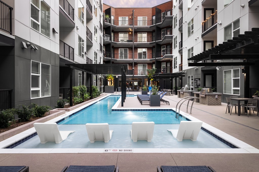 A pool surrounded by white chairs and buildings.
