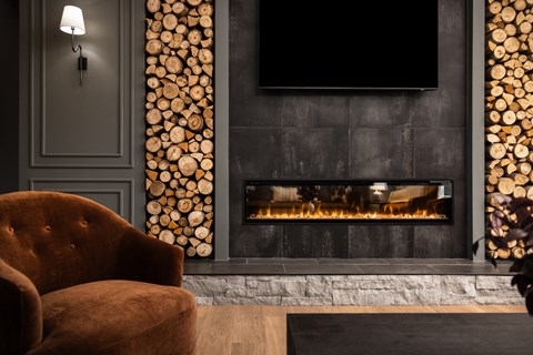 A fireplace with logs on the side and a chair in front.