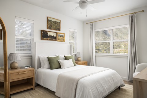 A bedroom with a large bed, a wooden nightstand, and a ceiling fan.