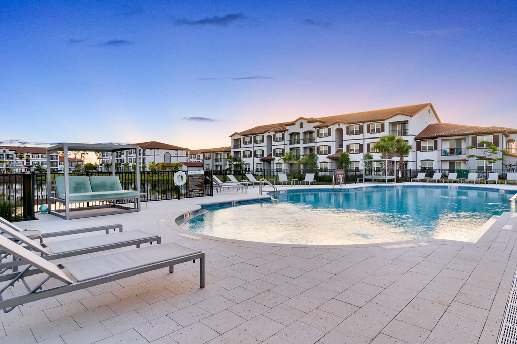 A large swimming pool surrounded by lounge chairs and a building in the background.