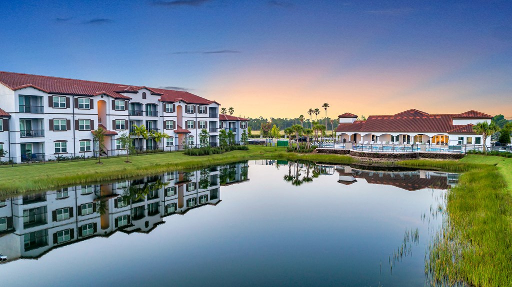 A serene scene of apartment buildings reflected in a calm body of water during sunset.