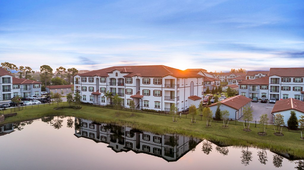 A serene lake reflects the buildings in the distance during a beautiful sunset.
