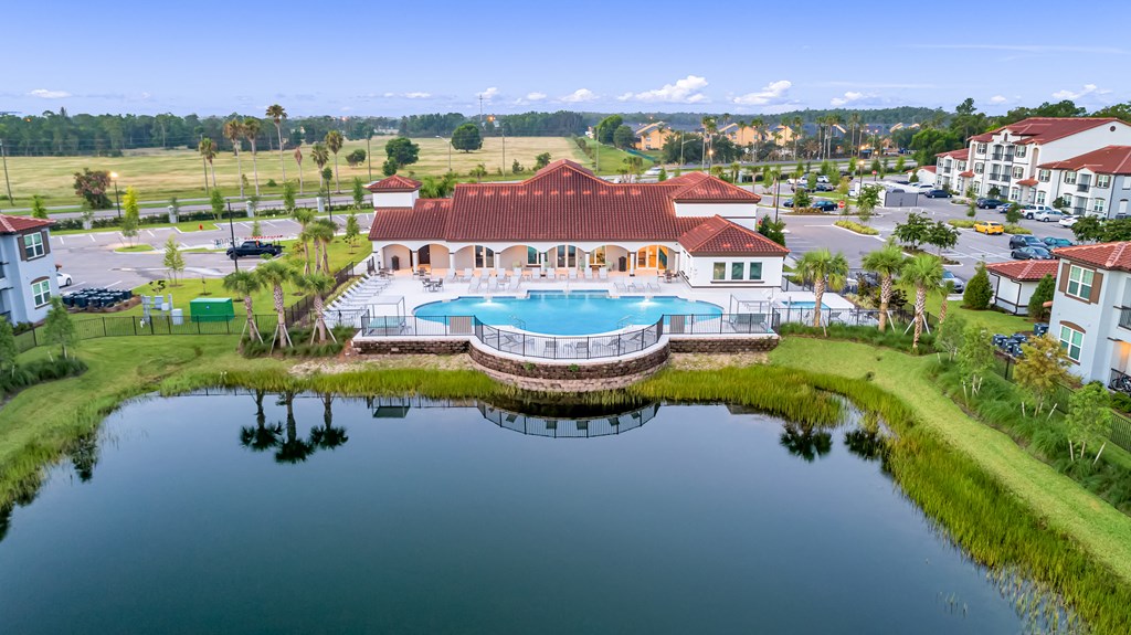 A large building with a red roof is surrounded by a pool and a pond.