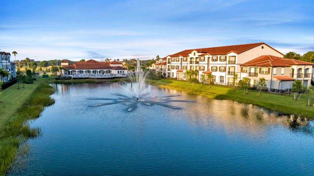 A fountain in the middle of a pond in front of a building.