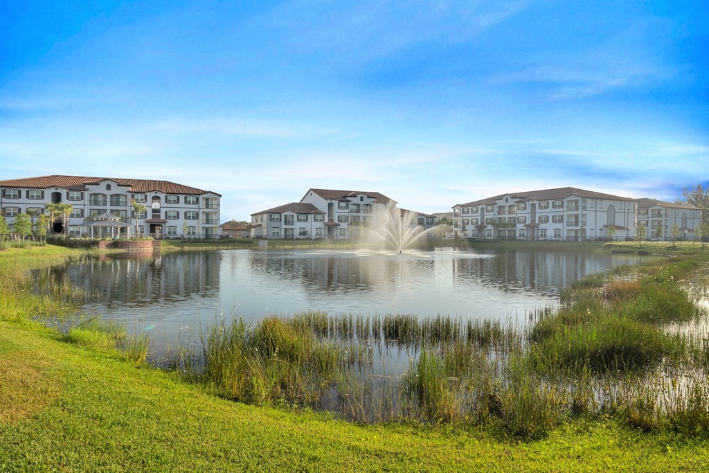 A serene lake with a fountain in the middle surrounded by buildings.