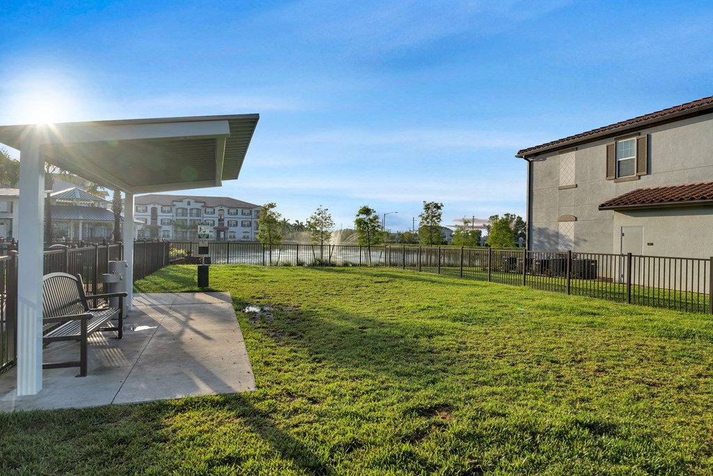 A sunny day at a park with a bench and a building in the background.