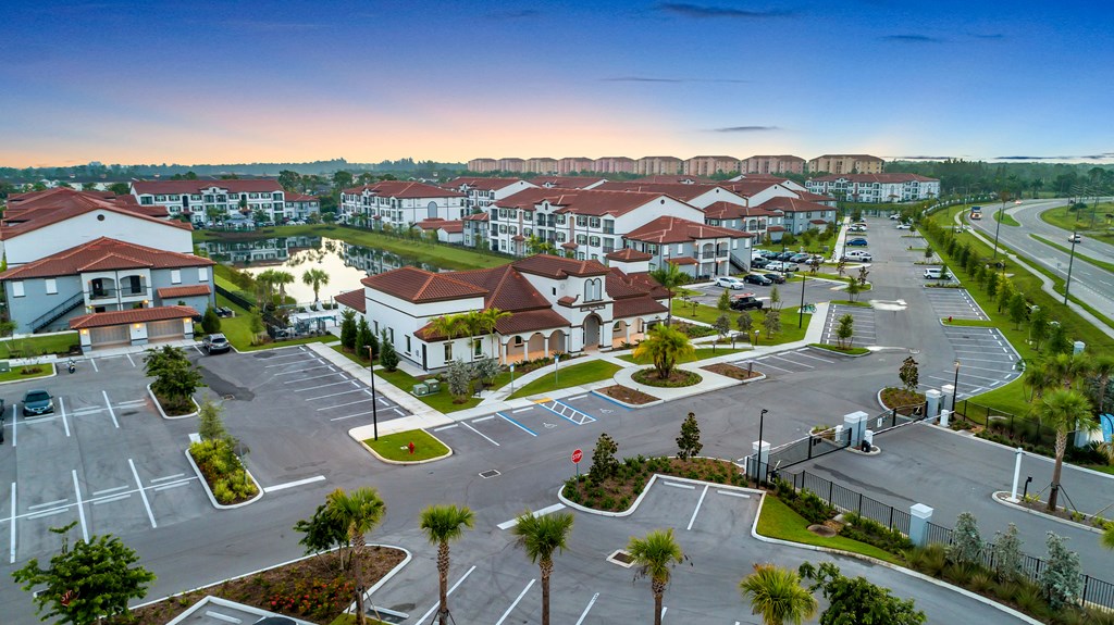 A sunset view of a residential complex with a parking lot in the foreground.
