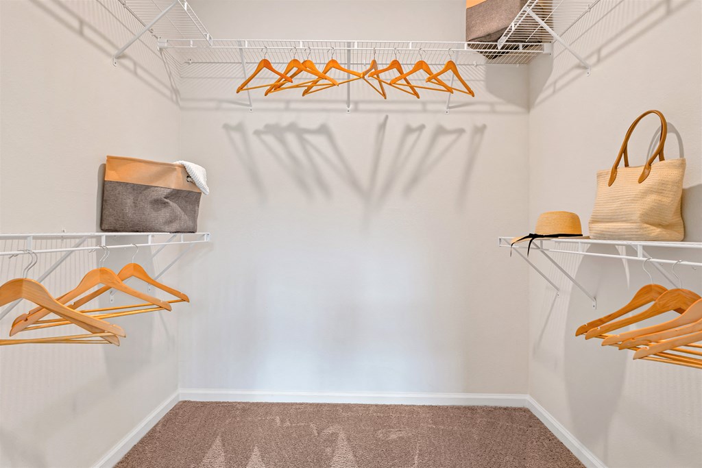 A room with white walls and a brown carpet with clothes hanging and a bag on a shelf.