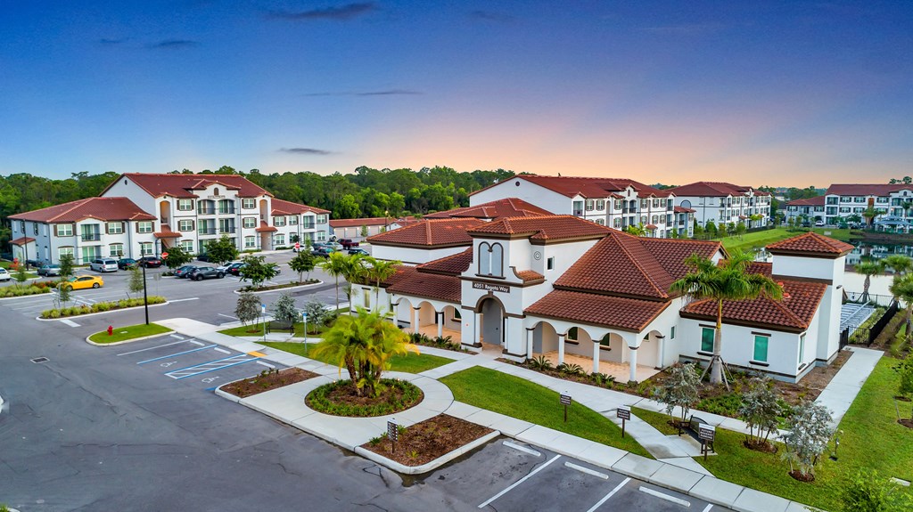 A large building with a red roof is surrounded by a parking lot.