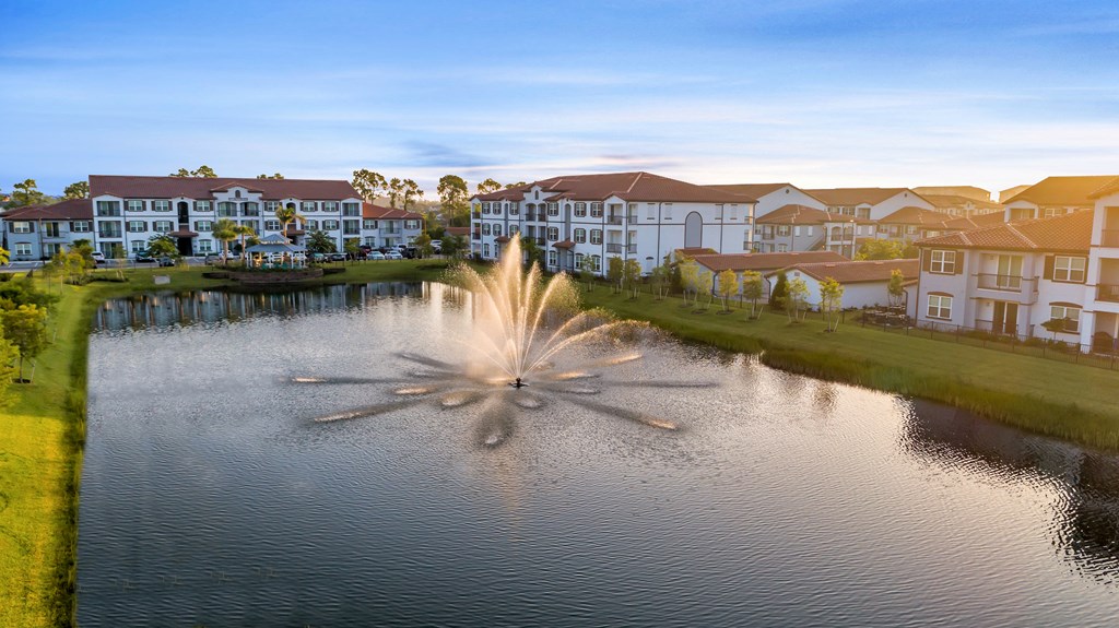 A fountain in the middle of a lake with houses in the background.