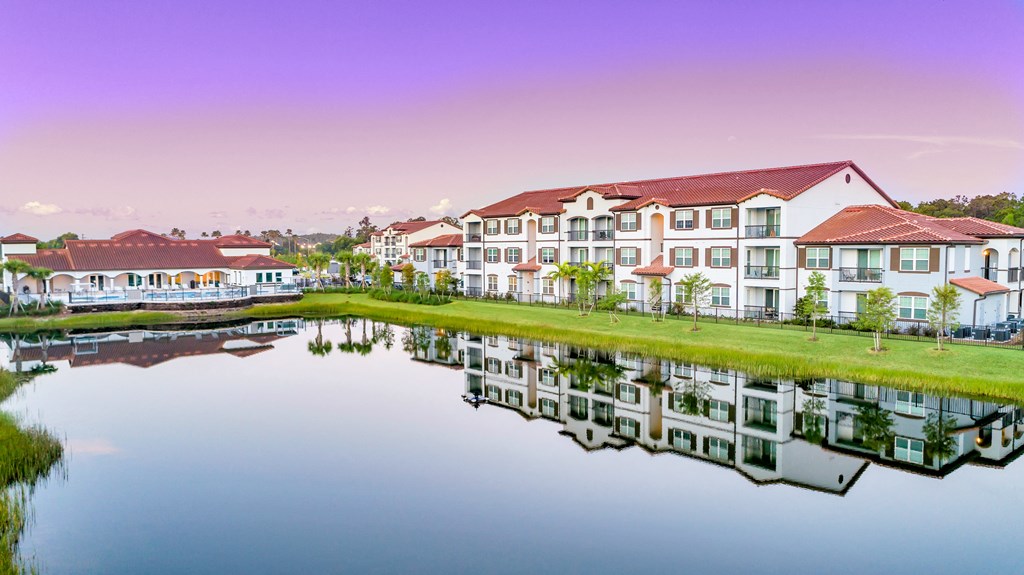 A serene scene of apartment buildings reflected in a calm body of water.