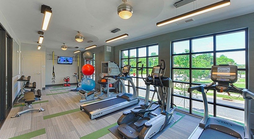 a gym with cardio equipment and large windows